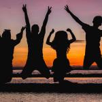 Silhouette of friends jumping on the beach at sunset, celebrating summer fun.
