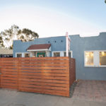 Front exterior of 3764 Alabama in North Park featuring a blue bungalow, a modern wood privacy fence, and a paved driveway under a clear sky.