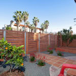 Private fenced patio at 3764 Alabama in North Park featuring a horizontal wood fence, terracotta tile walkway, citrus trees, and raised garden beds under a clear blue sky.