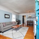 View from a bright blue front door at 3764 Alabama in North Park into a cozy living area with a grey sofa, geometric rug, and hardwood floors.