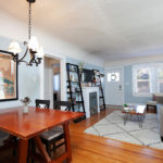 Modern open-concept living and dining space at 3764 Alabama in North Park with warm hardwood floors, a vintage-style chandelier, and a bright living area featuring a fireplace and large windows.
