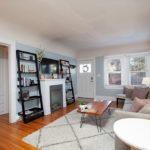 Inviting living room at 3764 Alabama in North Park featuring built-in hallway storage, a grey sofa with plush pillows, and a white fireplace flanked by black ladder shelving.