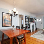 Open-concept living and dining space at 3764 Alabama St in North Park featuring light blue walls, original hardwood floors, a cozy dining set with a classic chandelier, and a decorative fireplace flanked by modern ladder bookshelves.