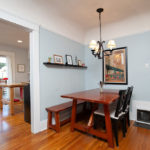 Dining area at 3764 Alabama St in North Park featuring a warm wood table with bench seating, a classic chandelier, light blue walls, and original hardwood floors that flow into the adjacent kitchen.
