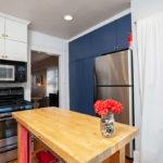 Updated kitchen at 3764 Alabama St in North Park featuring navy blue floor-to-ceiling cabinetry, stainless steel appliances, and a butcher block island with a vibrant floral centerpiece.