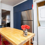 Updated kitchen at 3764 Alabama St in North Park featuring a butcher block island, stainless steel appliances, navy blue floor-to-ceiling cabinetry, and a convenient in-unit stacked washer and dryer.