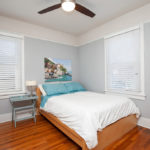Light-filled bedroom at 3764 Alabama St in North Park featuring original hardwood floors, soft grey walls with classic white trim, and large windows with white blinds.