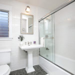 Bright, updated bathroom at 3764 Alabama St in North Park featuring classic white subway tile, a pedestal sink, and a glass-enclosed bathtub and shower.