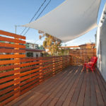 Elevated wooden deck at 3764 Alabama St in North Park featuring modern horizontal slat railings, bright red Adirondack chairs, and a white sun shade sail against a clear blue sky.