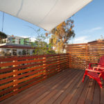 Elevated wood deck at 3764 Alabama St in North Park featuring modern horizontal slat railings, vibrant red Adirondack chairs, and a white sun shade under a clear sky.