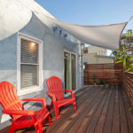 Spacious wood deck at 3764 Alabama St in North Park featuring bright red Adirondack chairs, a white sun shade sail, and a modern horizontal privacy fence.