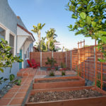 Urban front yard at 3764 Alabama St in North Park featuring wooden raised garden beds, a Saltillo tile walkway, and a modern horizontal slat fence under a clear blue sky.