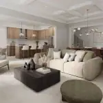 Interior view of an open-concept living area and kitchen at The Heights of Harmony East, showcasing a coffered ceiling, wood cabinetry, a large kitchen island with white stools, and modern neutral furniture.