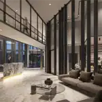 Luxury lobby interior at The Wilmot Condos featuring a marble concierge desk, high ceilings with floor-to-ceiling glass partitions, a modern fireplace lounge, and polished stone flooring.