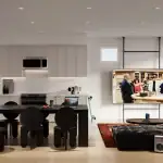 Brooklin Towns - KitchenLiving Open-concept kitchen and living area at Brooklin Towns featuring minimalist white cabinetry, a black dining set, and a contemporary lounge space with a retro boombox and ring light.