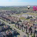 Aerial drone view of the New Kleinburg master-planned suburban housing development, showcasing rows of modern homes, a community school, local green spaces, and map markers indicating proximity to the Highway 427 off-ramp and on-ramp.