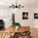 Modern open-concept kitchen and dining area at Creekside Trail featuring white cabinetry, subway tile backsplash, stainless steel appliances, and a round wooden dining table with wishbone chairs under a black minimalist chandelier.