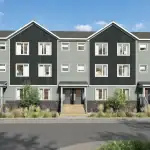 Front streetscape view of modern townhouses at The Grove Townhomes at Wildflower, showcasing multi-toned grey facades, gabled roofs, stone foundations, and pedestrian walkways with native landscaping.