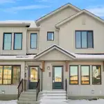 Exterior of modern townhomes at Desrochers Villages in the winter, showing light beige vertical siding, dark window frames, and snow-covered steps leading to front doors.