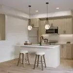 East Hills Crossing - Kitchen Modern open-concept kitchen at East Hills Crossing featuring light wood cabinetry, a white quartz waterfall island with seating, stainless steel appliances, and contemporary globe pendant lighting.