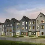 Exterior rendering of Poppy at Rangeview modern townhomes featuring multi-colored facades in blue, grey, and cream with gabled roofs and manicured landscaping under a sunset sky.