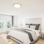 Spacious, bright bedroom at Riverbend Townhomes with light wood flooring, neutral white walls, large windows overlooking greenery, and minimalist modern furniture.
