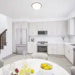Interior view of a modern Riverbend Townhomes kitchen featuring light wood-grain cabinetry, white countertops, stainless steel appliances, and a nearby carpeted staircase with dark wood railings.