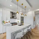 Fifth Avenue Homes Woodbridge - Kitchen Modern luxury kitchen at Fifth Avenue Homes Woodbridge with white cabinetry, a large waterfall island, gold hardware, and high-end stainless steel appliances.