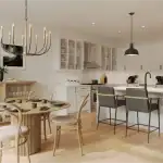 Modern open-concept kitchen and dining area at Heartwood Village featuring white cabinetry, a large island with breakfast seating, light wood flooring, and a contemporary chandelier over a round wooden dining table.