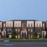 Architectural rendering of Sol Stacked Towns exterior featuring modern multi-level brick and stone facades with landscaped front yards and clean architectural lines under a clear twilight sky.