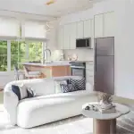 Bright, open-concept interior rendering of an OG Urban Towns unit, showcasing a modern kitchen with light cabinets and stainless steel appliances, a cozy dining area, and a contemporary living room with a white sofa.