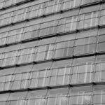 Schwarz-weisse Glasfassade mit repetitiver Rasterstruktur als Metapher für Plausibilität, glatten Output und ungeprüfte Qualität durch KI in Unternehmen