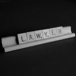 Scrabble tiles on a rack spelling out the word "LAWYER" against a black background.