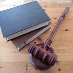 Wooden gavel resting on its sound block next to two stacked books on a wooden table.