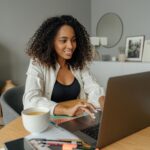 A designer at a desk with a laptop, surrounded by tools of her trade and a cup of coffee