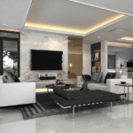 A modern living room with white sofas, a black ottoman, a large TV mounted on a marble wall, and a dining area with chairs and a table in the background.