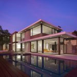 Modern residential home featuring sleek architecture and large glass windows at dusk.