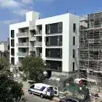 Contemporary white apartment building with large black framed windows and open balconies, modern minimalist style, under construction.