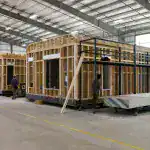 Wooden building framework with steel scaffolding in an industrial warehouse.