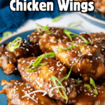 A blue plate piled high with glossy, sticky Chinese Chicken Wings garnished with sesame seeds and green onions.