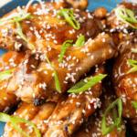 close-up of the sticky, dark glaze on a chicken wing, showing the texture of the sauce and sesame seeds.