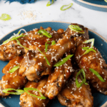 plate of glazed Chinese wings with a blue napkin in the background.