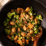 A white plate featuring a portion of honey garlic chicken and steamed broccoli florets next to a silver fork.
