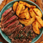 Close up of sliced steak topped with green chimichurri sauce and served with garlic fries.
