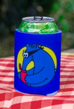 Blue Aardvark Koozie on red picnic table with greenery in the background.
