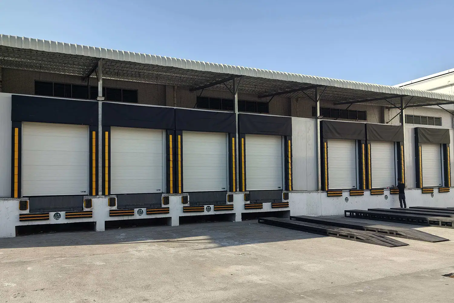 Exterior view of a modern logistics center featuring a row of commercial dock high doors integrated with heavy-duty dock seals and levelers. ABX OEM manufacturer provides CE/ISO certified loading bay integration solutions for global wholesale projects.