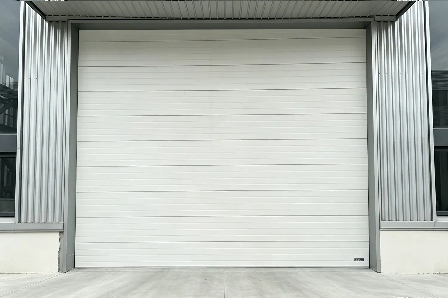White commercial sectional overhead door installed on a modern industrial warehouse with corrugated metal siding and an overhead canopy.