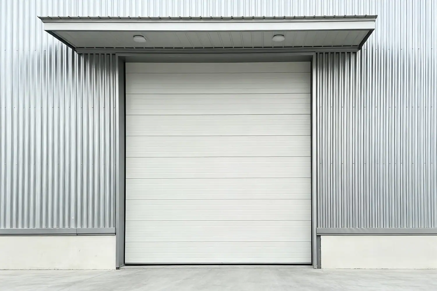 White commercial sectional overhead door installed on a modern industrial warehouse with corrugated metal siding and an overhead canopy.