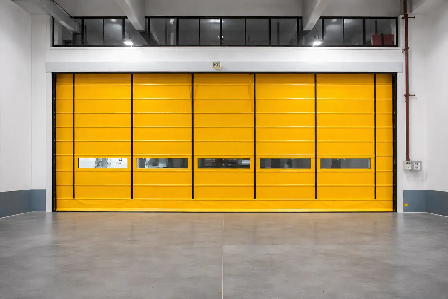 Wide yellow high-speed stacking door featuring prominent vertical lifting straps and segmented vision windows, used for environmental separation within a heavy manufacturing plant.