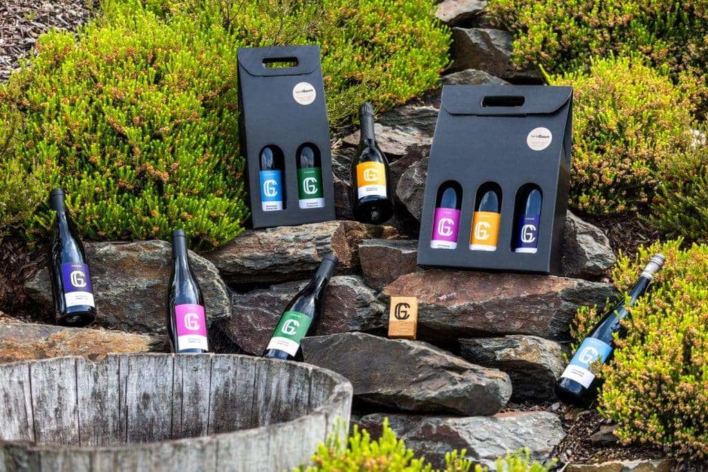 Weinflaschen mit bunten Etiketten auf Steinen und in Geschenkkartons, outdoor.